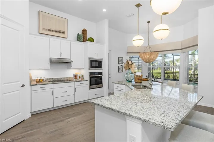 Kitchen with light wood finished floors, black appliances, white cabinetry, a large island, and hanging light fixtures
