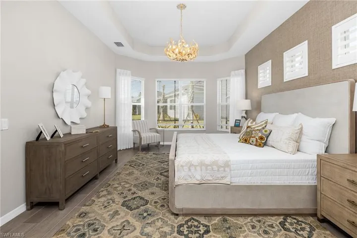 Bedroom featuring a raised ceiling, a chandelier, and wood finished floors