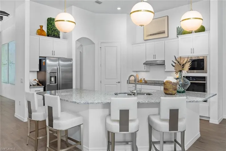 Kitchen with wood finished floors, stainless steel appliances, arched walkways, white cabinets, and recessed lighting