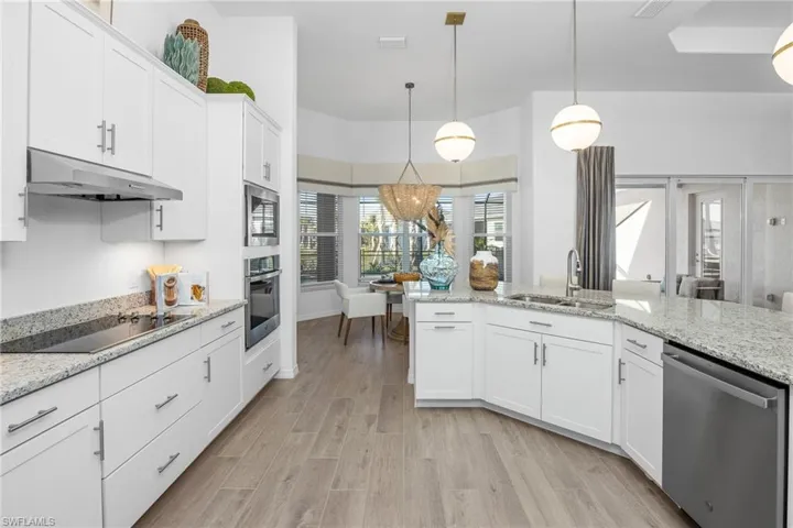 Kitchen with appliances with stainless steel finishes, under cabinet range hood, white cabinets, hanging light fixtures, and light wood-style flooring