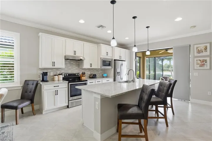 Kitchen with stainless steel appliances, ornamental molding, a breakfast bar, light stone counters, and tasteful backsplash