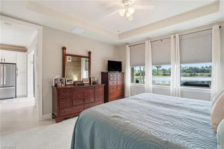 Bedroom with freestanding refrigerator, a tray ceiling, ceiling fan, and light tile patterned floors