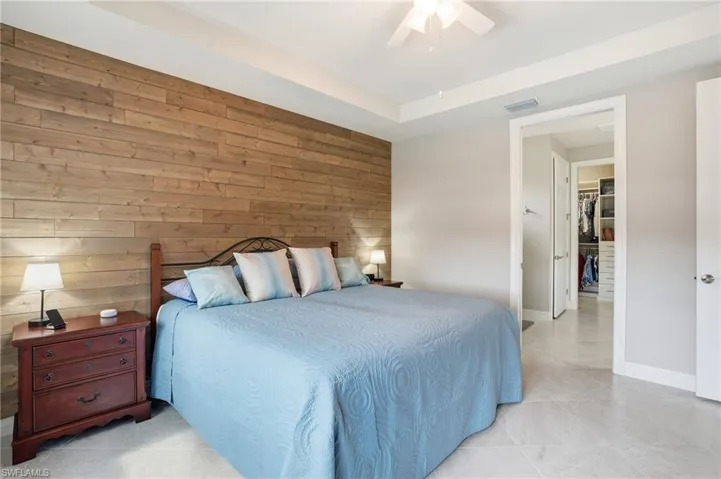 Bedroom featuring wooden walls, a ceiling fan, light tile patterned flooring, and a tray ceiling