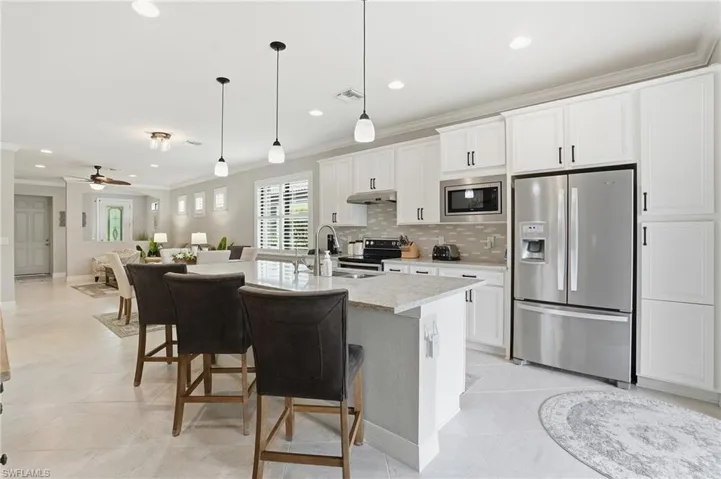 Kitchen featuring ornamental molding, appliances with stainless steel finishes, decorative backsplash, open floor plan, and white cabinets