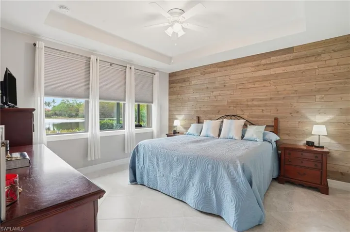 Bedroom featuring wooden walls, a raised ceiling, light tile patterned flooring, and a ceiling fan