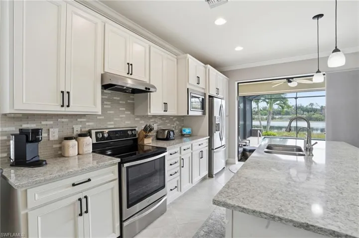 Kitchen with stainless steel appliances, hanging light fixtures, light stone counters, tasteful backsplash, and crown molding