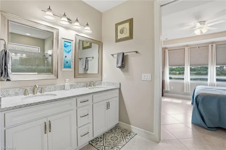 Bathroom featuring double vanity, light tile patterned flooring, ceiling fan, ensuite bath, and tiled shower