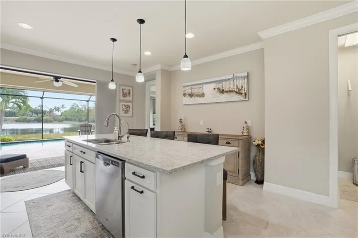 Kitchen with light stone counters, white cabinetry, ceiling fan, light tile patterned floors, and a center island with sink