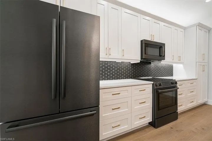 Kitchen with black appliances, white cabinets, light wood-style floors, tasteful backsplash, and light stone countertops