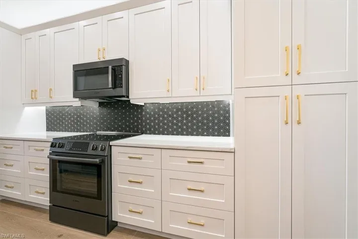 Kitchen with stainless steel electric stove, white cabinets, tasteful backsplash, light stone counters, and light wood-style flooring