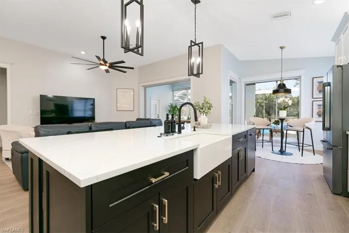 Kitchen with dark cabinetry, decorative light fixtures, high quality fridge, a kitchen island with sink, and open floor plan