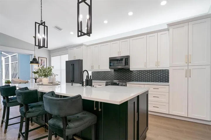 Kitchen featuring hanging light fixtures, stainless steel appliances, light stone countertops, a kitchen island with sink, and dual tone cabinetry