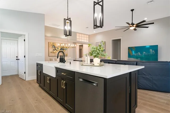 Kitchen featuring dark cabinets, dishwasher, a center island with sink, open floor plan, and light stone counters