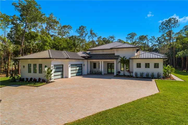 View of front of home featuring stucco siding, decorative driveway, a garage, a front lawn, and a standing seam roof