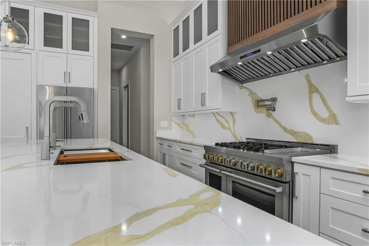 Kitchen with light stone countertops, high end appliances, white cabinets, and glass fronted cabinets