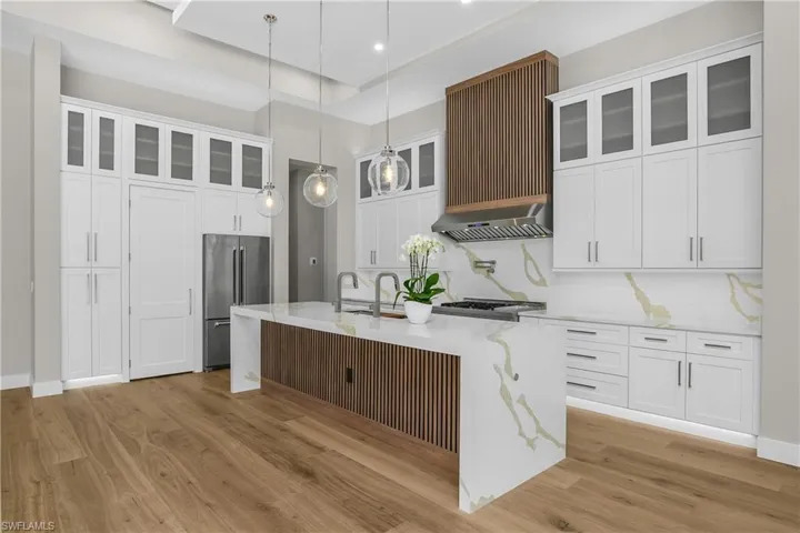 Kitchen with light stone counters, white cabinets, pendant lighting, and high end refrigerator