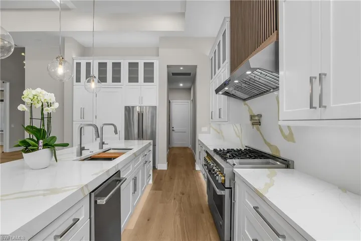 Kitchen with light stone countertops, stainless steel appliances, white cabinets, light wood-type flooring, and pendant lighting