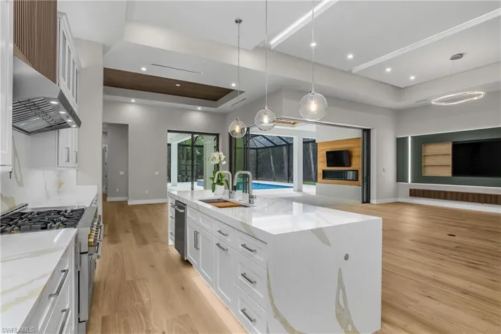 Kitchen featuring white cabinetry, light stone countertops, open floor plan, stainless steel appliances, and a raised ceiling