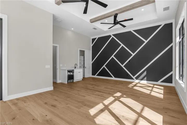 Unfurnished living room featuring an accent wall, light wood finished floors, recessed lighting, a ceiling fan, and beamed ceiling