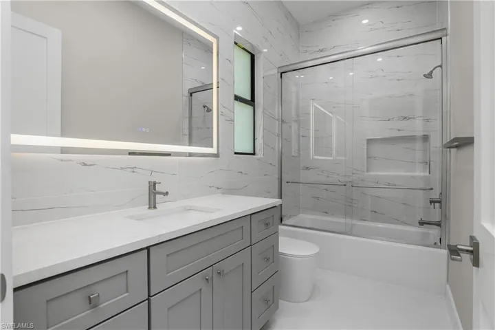 Bathroom with combined bath / shower with glass door, vanity, and tile walls
