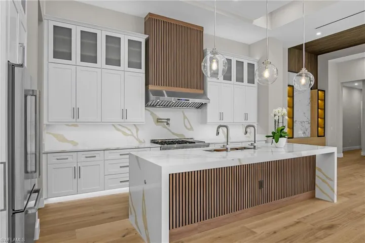 Kitchen featuring white cabinetry, light wood-type flooring, light stone countertops, and pendant lighting