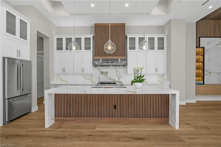 Kitchen featuring high end fridge, glass insert cabinets, light wood-style floors, light stone countertops, and white cabinetry