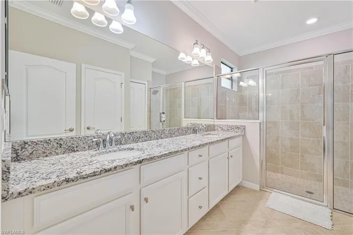 Full bath with crown molding, double vanity, a shower stall, and a sink