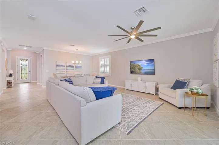 Living area featuring visible vents, baseboards, ornamental molding, light tile patterned floors, and ceiling fan with notable chandelier
