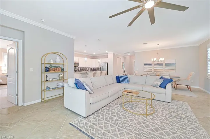 Living room with light tile patterned flooring, ceiling fan with notable chandelier, crown molding, and baseboards
