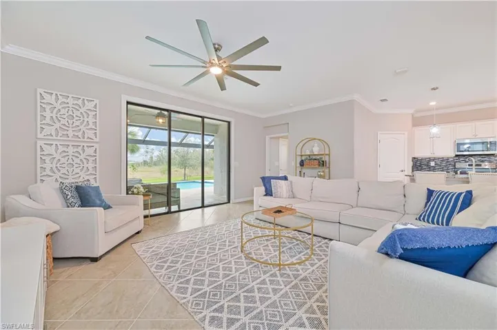 Living room with crown molding, light tile patterned flooring, a ceiling fan, and baseboards