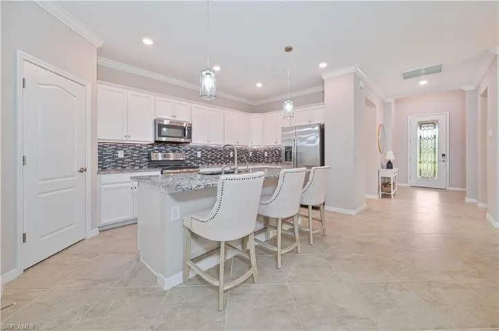 Kitchen with a center island with sink, visible vents, ornamental molding, appliances with stainless steel finishes, and tasteful backsplash