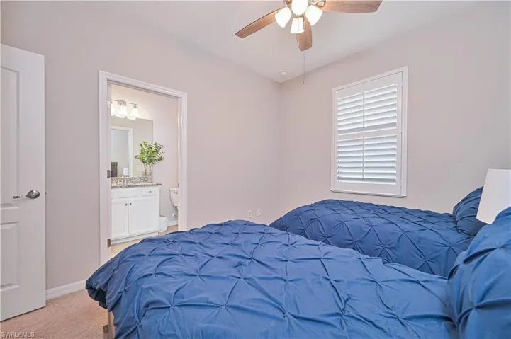 Carpeted bedroom with ensuite bath, baseboards, and a ceiling fan