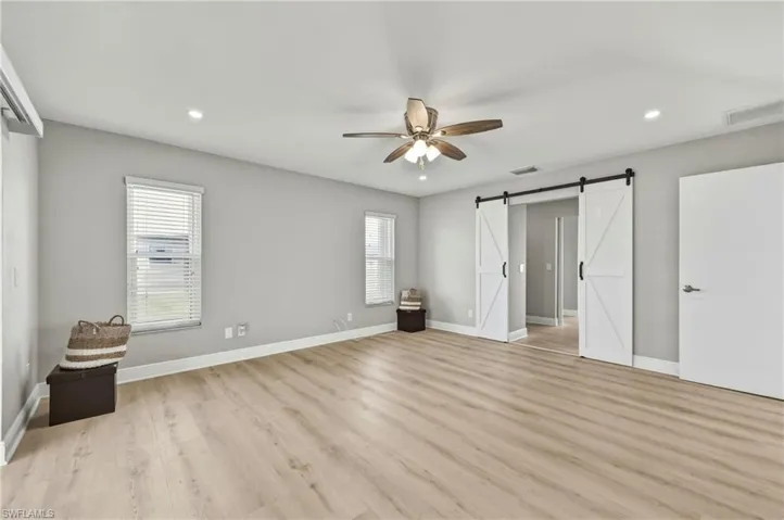 Unfurnished bedroom featuring a barn door, light wood-style flooring, recessed lighting, a ceiling fan, and multiple windows