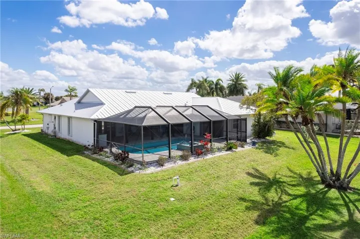 Rear view of house with an outdoor pool, a lanai, a lawn, and a sunroom