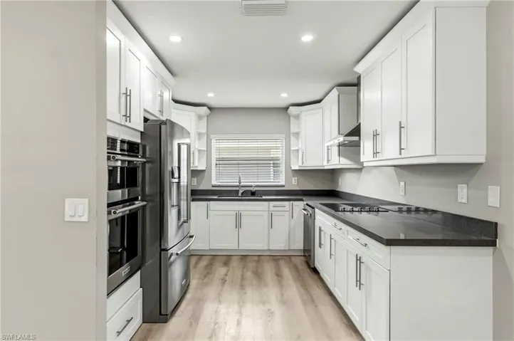 Kitchen with open shelves, stainless steel appliances, light wood-type flooring, white cabinets, and recessed lighting