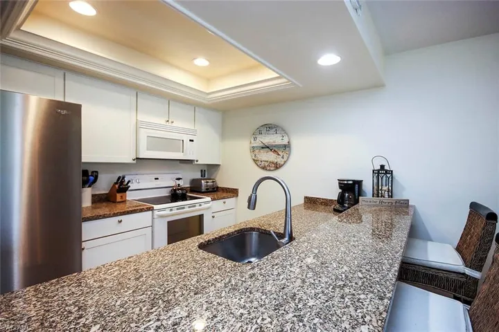 Kitchen with white appliances, dark stone countertops, recessed lighting, white cabinets, and a raised ceiling