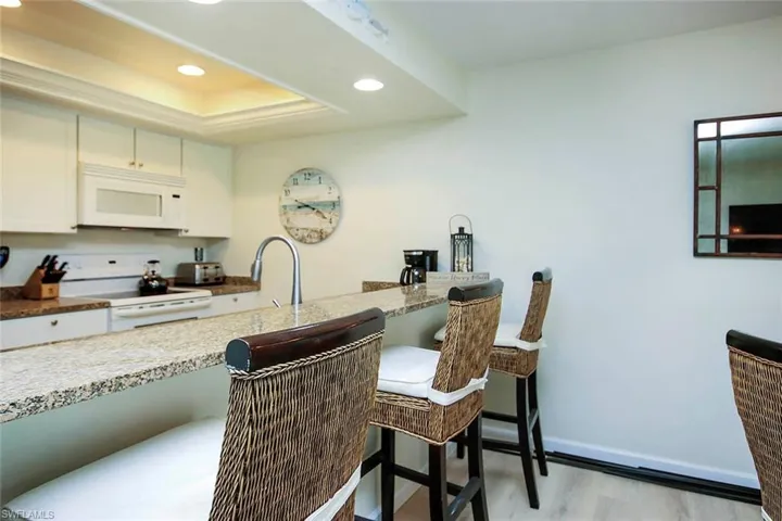 Kitchen with white cabinetry, white appliances, recessed lighting, light stone countertops, and light wood-style flooring