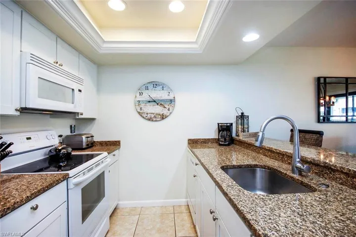 Kitchen featuring white appliances, white cabinets, dark stone counters, recessed lighting, and a tray ceiling