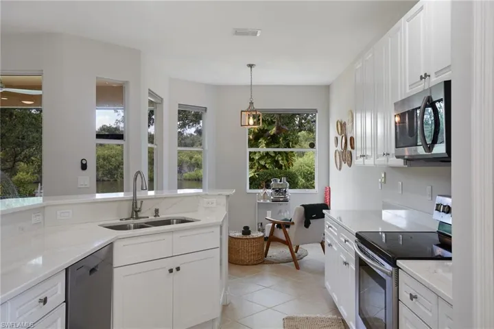 Contemporary kitchen featuring white cabinetry, light-toned countertops, a double basin sink with a gooseneck faucet, a stainless steel microwave, and integrated tile flooring