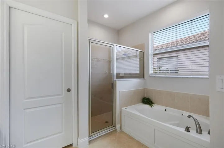 Bathroom featuring a built-in tub with tile surround, a separate glass-enclosed shower, a large window with blinds, and recessed lighting