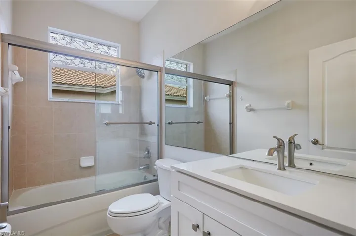 Bathroom featuring a tub/shower combination with sliding glass doors, neutral tile surround, and an integrated showerhead