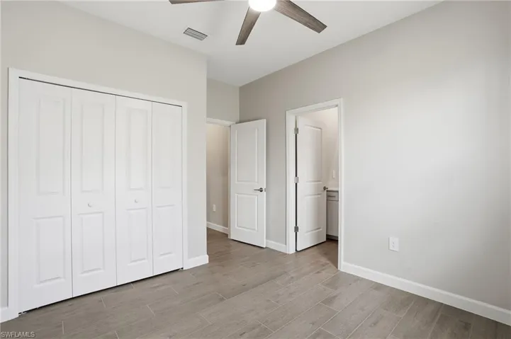 Unfurnished bedroom featuring wood tiled floors, a ceiling fan, a closet, and ensuite bathroom