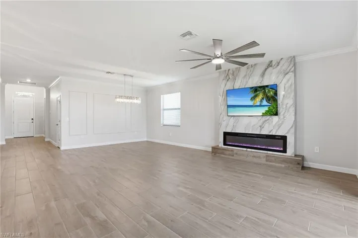 Unfurnished living room with a premium fireplace, crown molding, a ceiling fan, light wood-style flooring, and suspended lighting