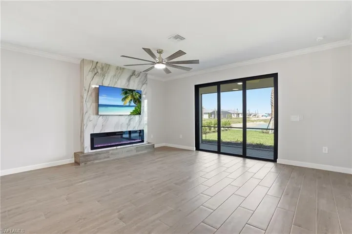 Unfurnished living room with wood finish floors, a high end fireplace, ceiling fan, plenty of natural light, and crown molding