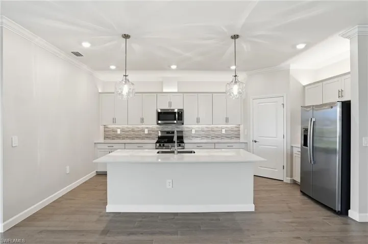 Kitchen with stainless steel appliances, light wood-style flooring, backsplash, a kitchen island with sink, and crown molding