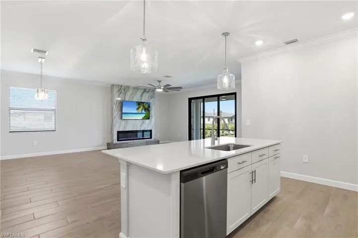 Kitchen with dishwasher, a kitchen island with sink, open floor plan, white cabinetry, and pendant lighting