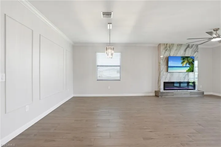 Unfurnished dining area with crown molding, light wood-style floors, a premium fireplace, ceiling fan, and suspended lighting