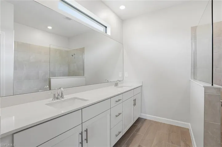 Bathroom featuring a walk in shower, double vanity, wood finish floors, and recessed lighting