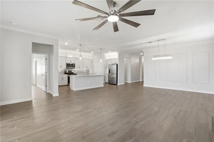 Unfurnished living room with crown molding, light wood finished floors, a ceiling fan, and a chandelier