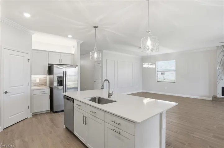 Kitchen with stainless steel appliances, light wood-style flooring, crown molding, a kitchen island with sink, and light stone counters